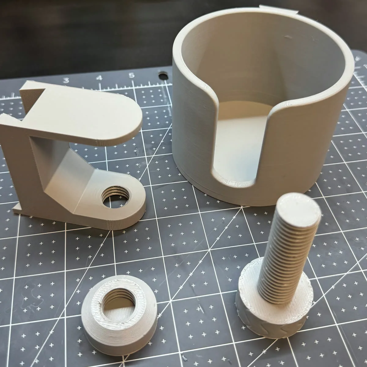 3D-printed modular cup holder prototype parts with threaded fastener and mounting bracket on a cutting mat
