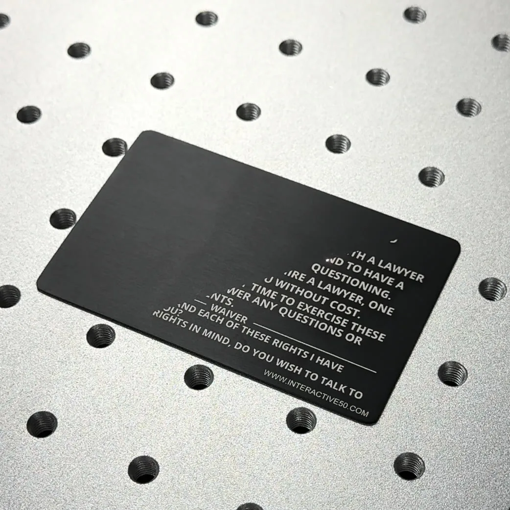 Fiber laser engraving Miranda rights text onto a black metal card